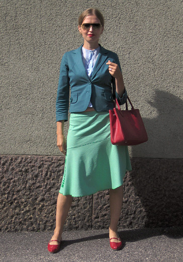 Woman wearing sunglasses, a pale blue blouse, a dark turquoise jacket, a turquoise green knee-length skirt and red court shoes. She's carrying a red handbag. (c) www.hel-looks.com